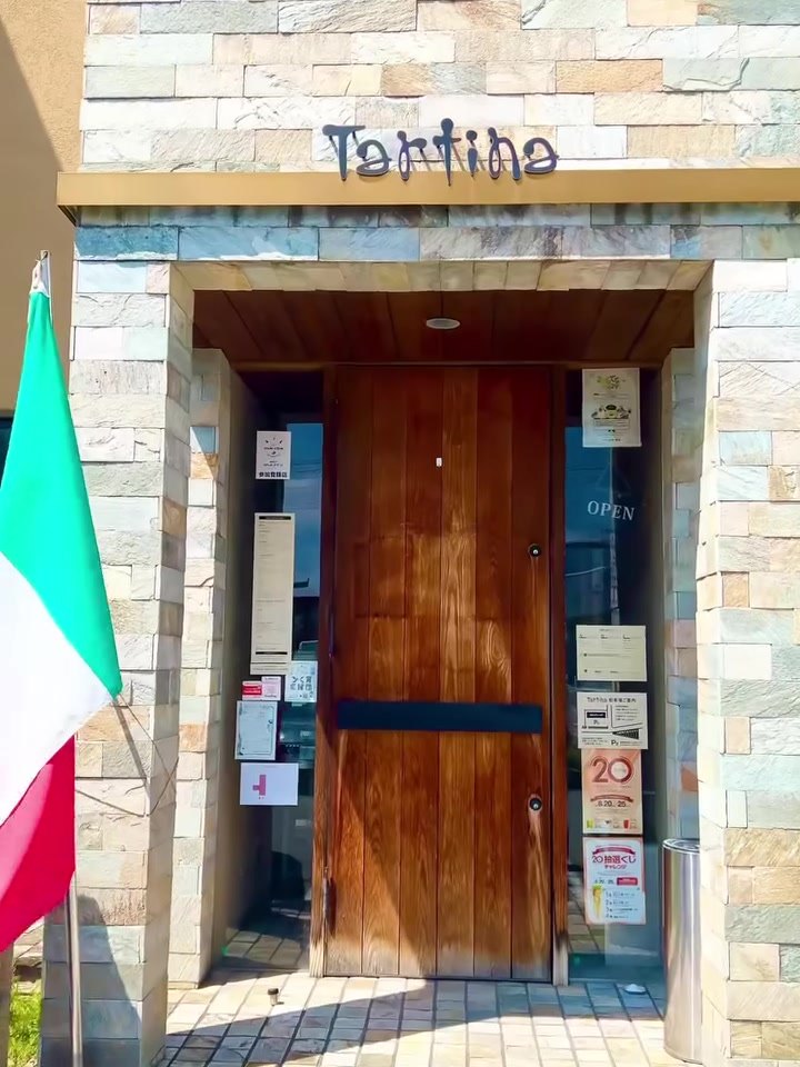tartina タルティーナの外観。石壁とイタリア国旗、木の扉